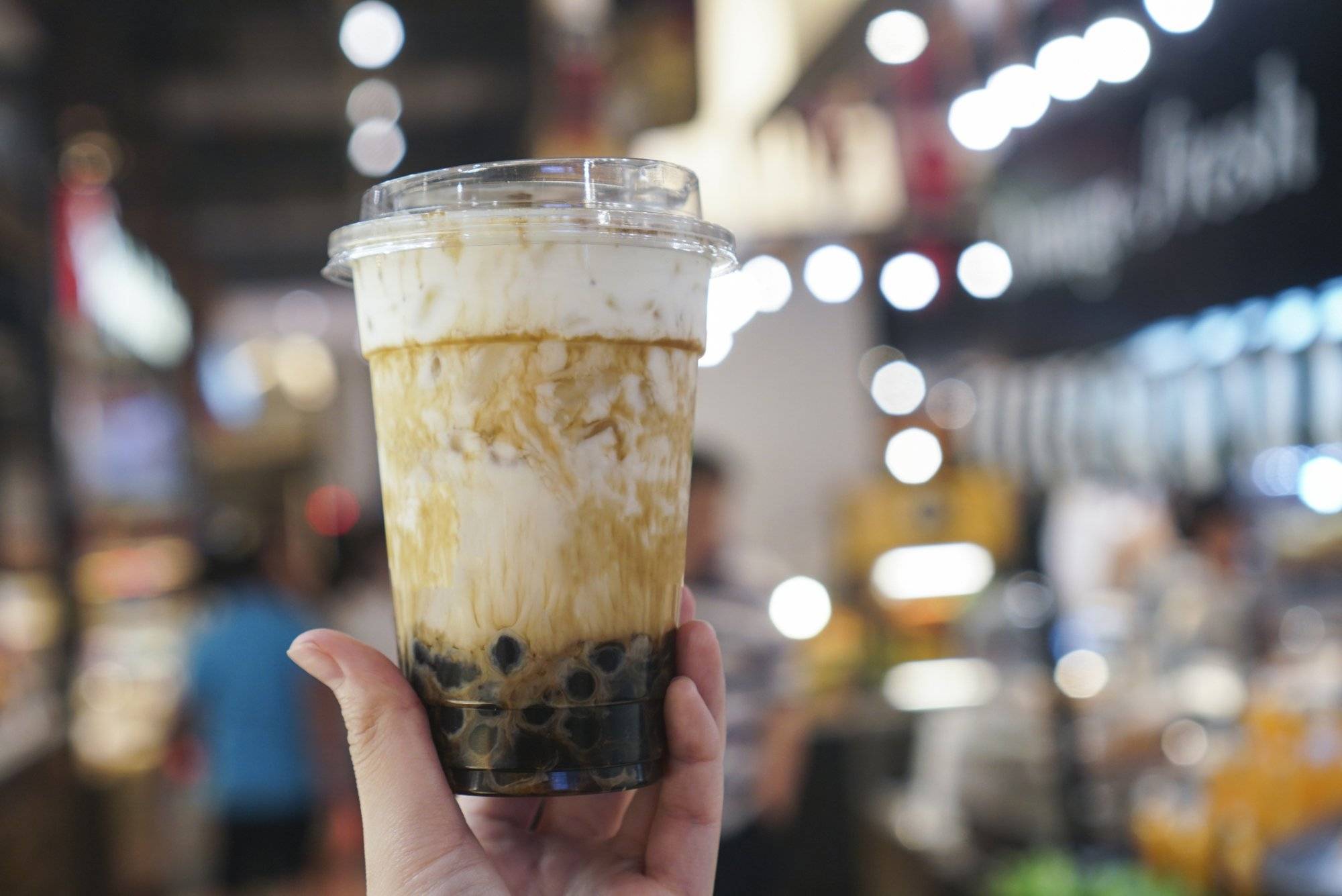 Hand holding a plastic cup of fresh milk with bubble/boba boiled in brown sugar.